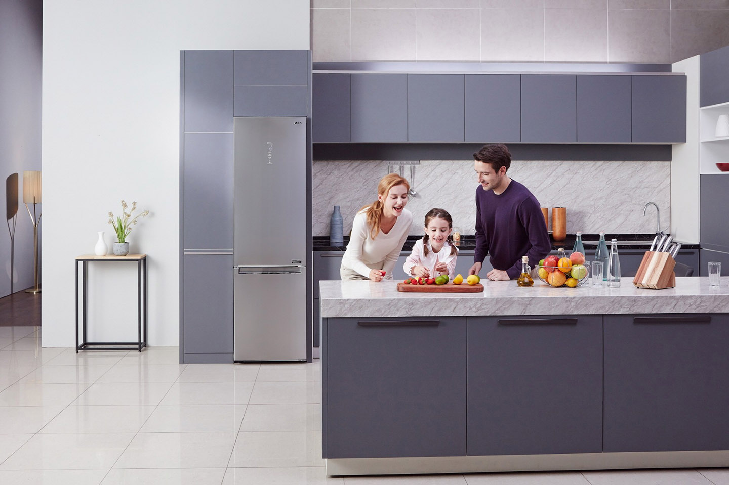 Little girl and her parents cutting fruit on the counter with LG Centum System™ bottom-freezer refrigerator in the background