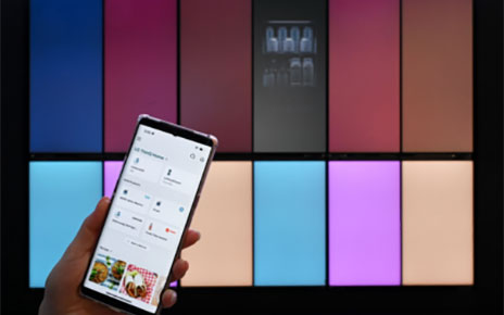 LG MoodUP fridges are exhibited at CES 2023 while a smartphone on the left side of the image displays LG ThinQ app