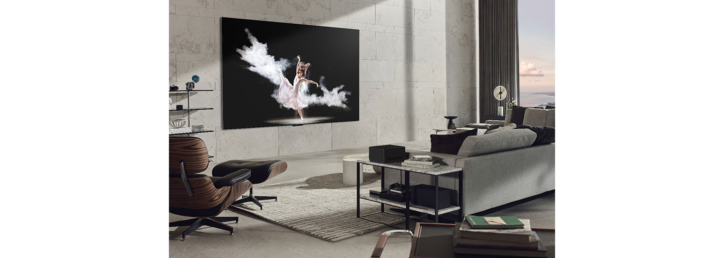 A wall-mounted LG SIGNATURE OLED M3 model displays an image of a woman performing ballet in a modern, gray-toned living room