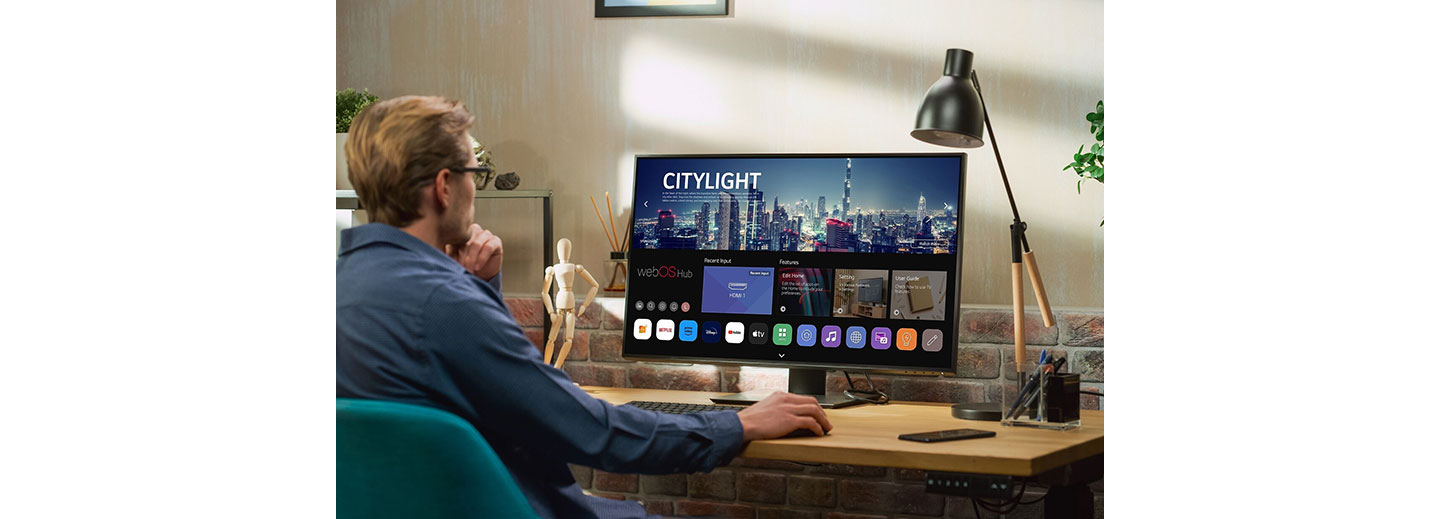 A man sitting at a desk explores the home UI of the new webOS Hub 2.0S on an LG smart monitor