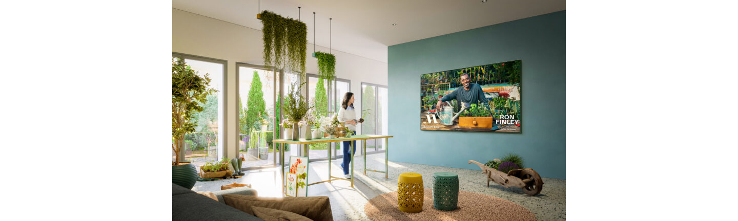 A woman watching a gardening lesson from the MasterClass app on her wall-mounted LG Smart TV as she tends to her plants