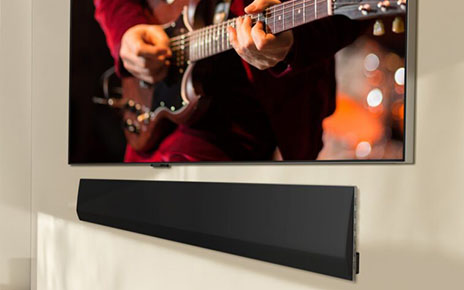 LG’s 2024 new soundbar model is wall mounted under an LG OLED TV that displays a man playing the guitar