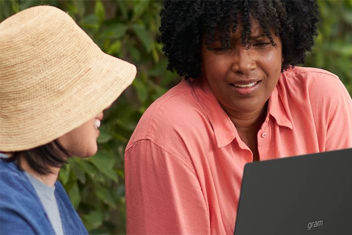 Two women are talking while using an LG gram with Windows 11.