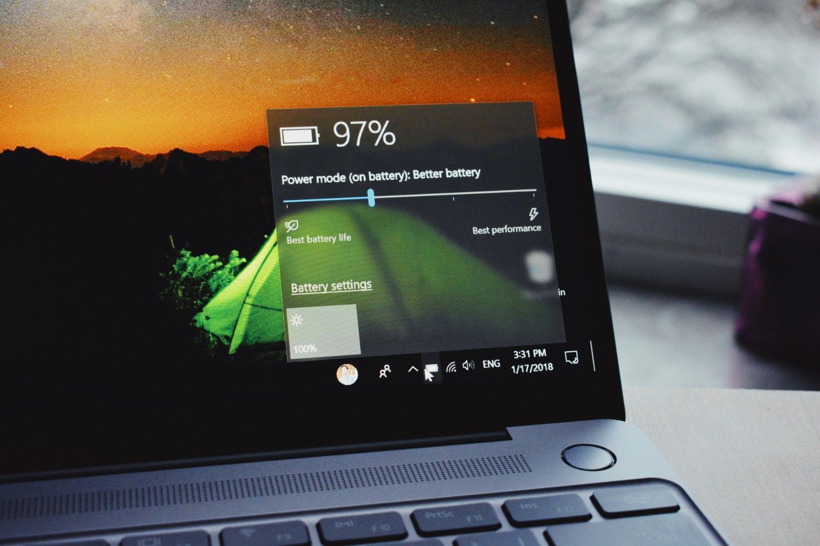 A laptop screen displaying a 97% battery status with power mode options, set against a sunset background wallpaper.