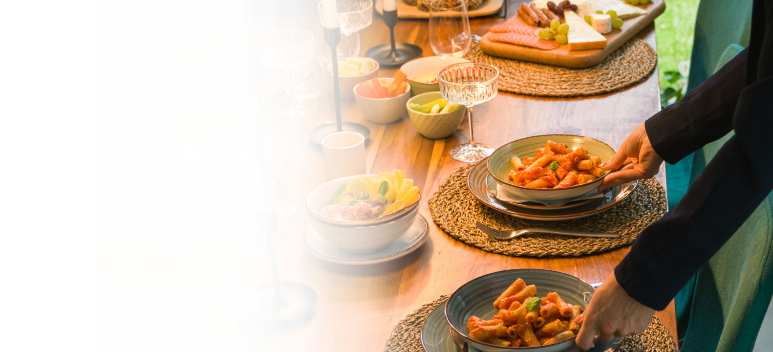 A woman preparing for a home party sets pasta on a dining table filled with food.