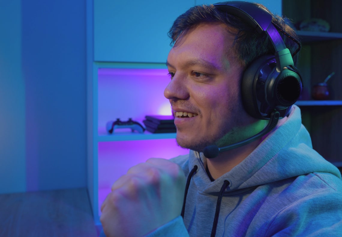 A gamer wearing a headset and a hoodie, looking excited during gameplay.