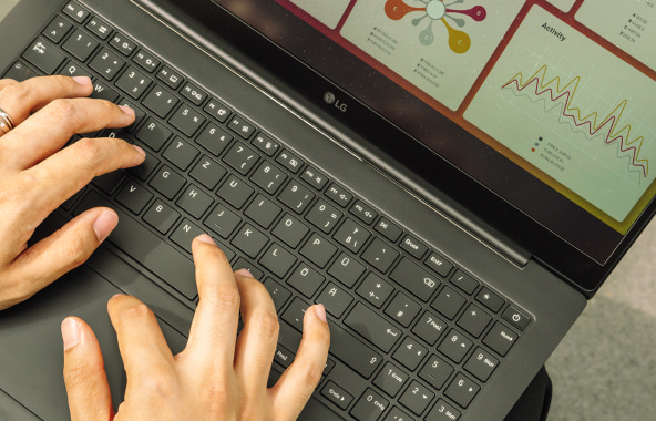 Close-up of hands typing on an LG gram Pro keyboard with charts displayed on the screen.