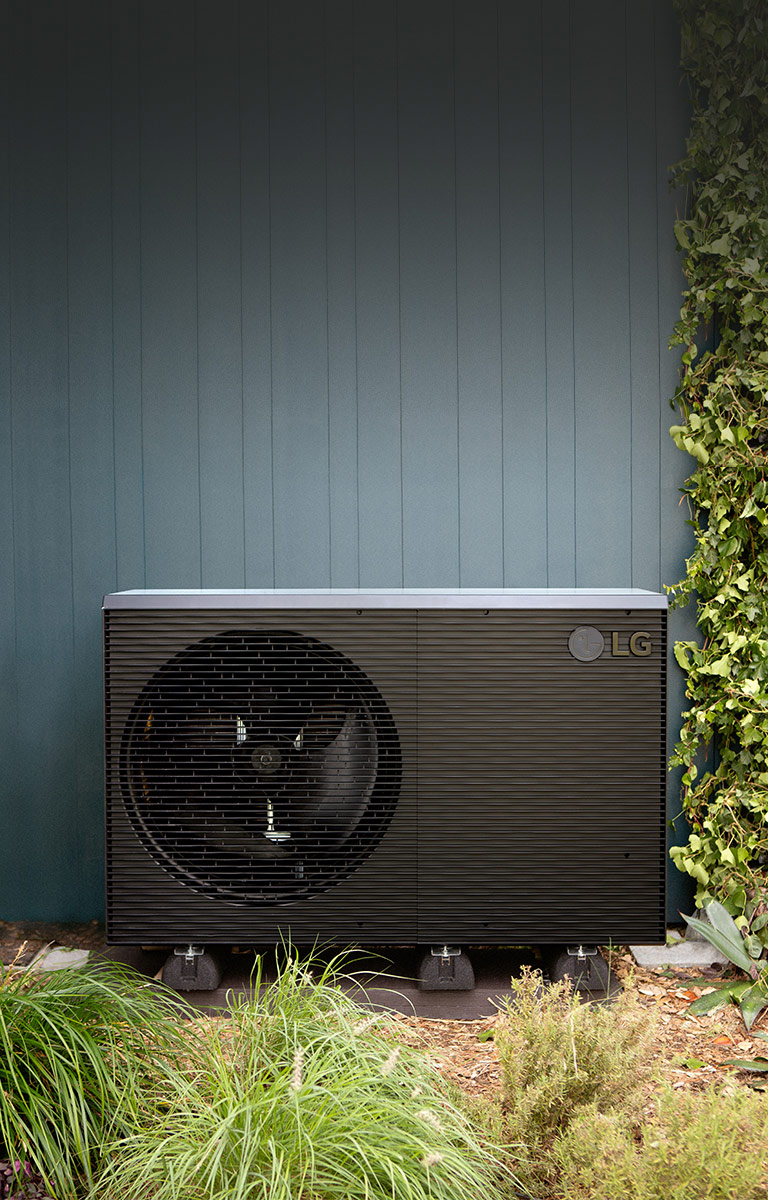 LG Air to Water Heat Pump THERMA V, black-colored outdoor unit is placed on the exterior wall of the house.	