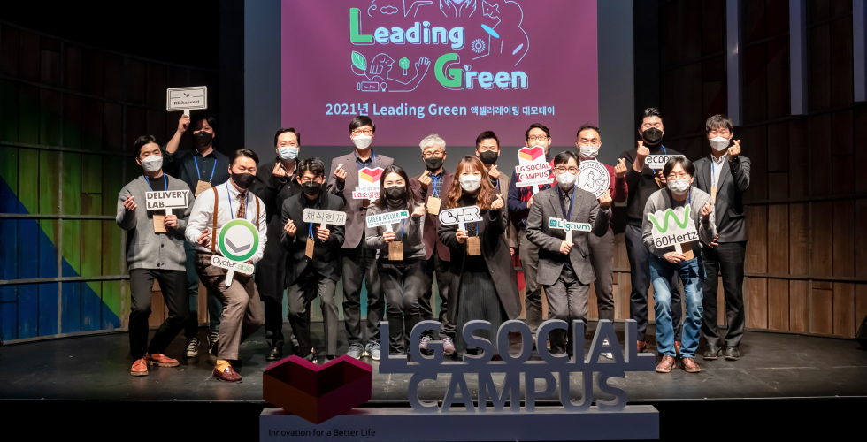 16 men and women who attended the LG Social Campus make a heart with their hands and take a group photo on the stage.